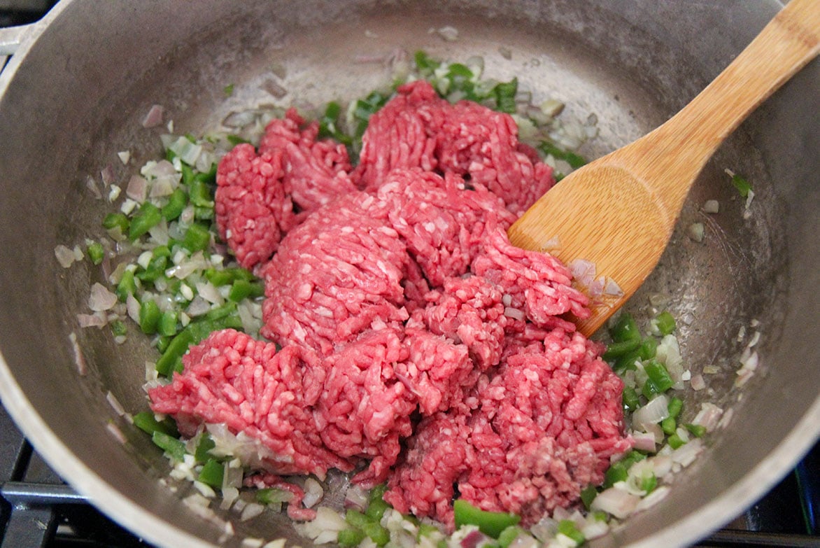onions, peppers, and ground beef in a skillet with a spoon