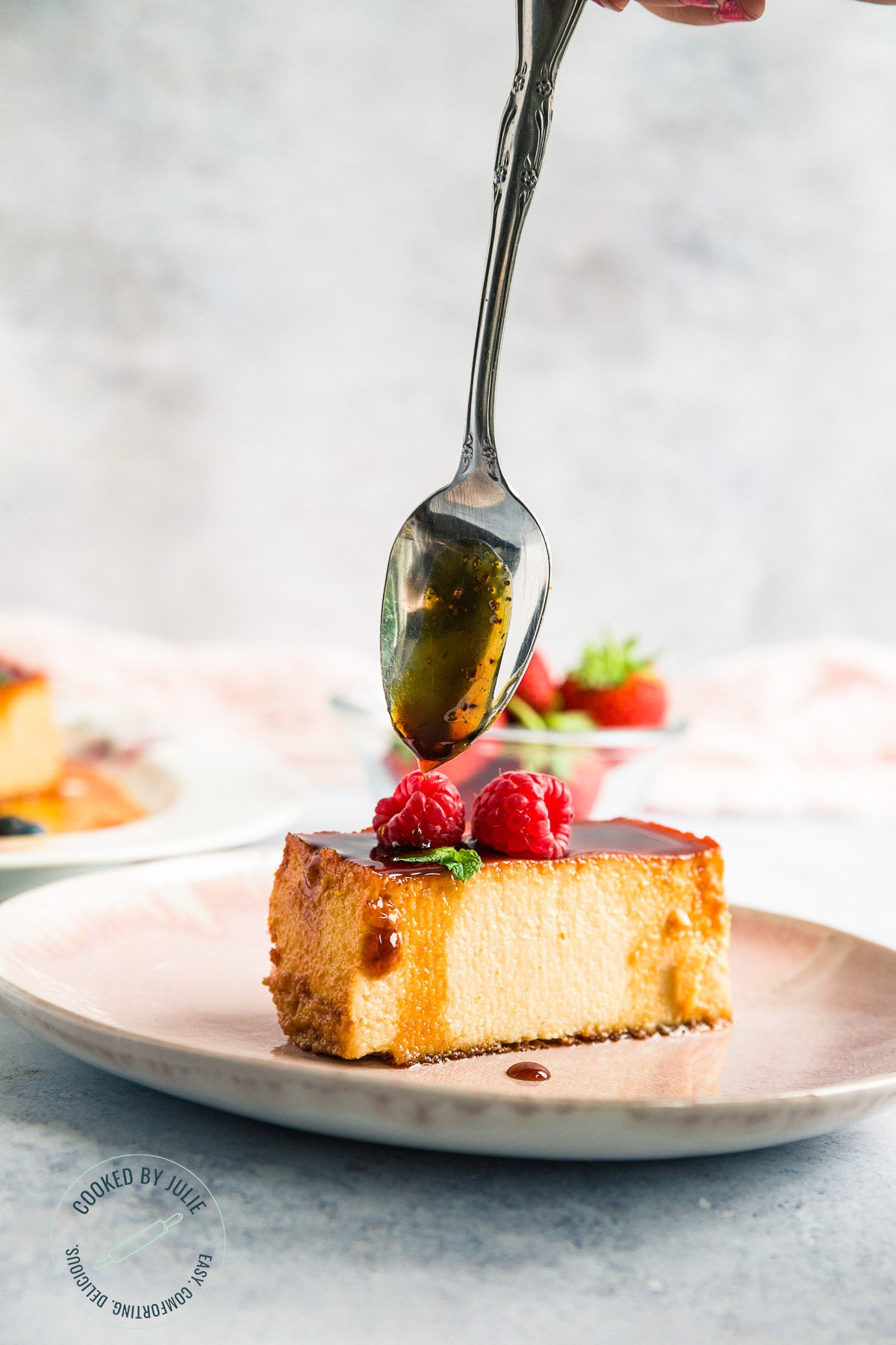 a slice of caramel custard on a pink plate with a spoon drizzling caramel over it. 