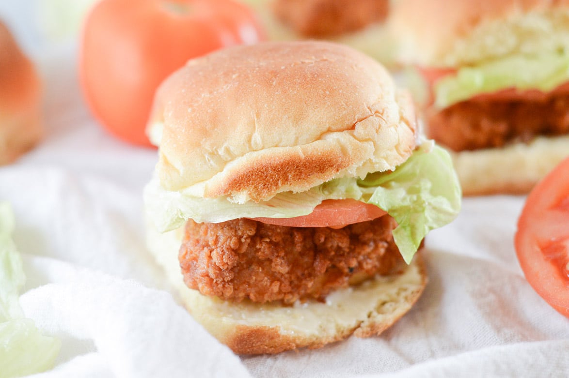 chicken slider with lettuce and tomato on a white surface