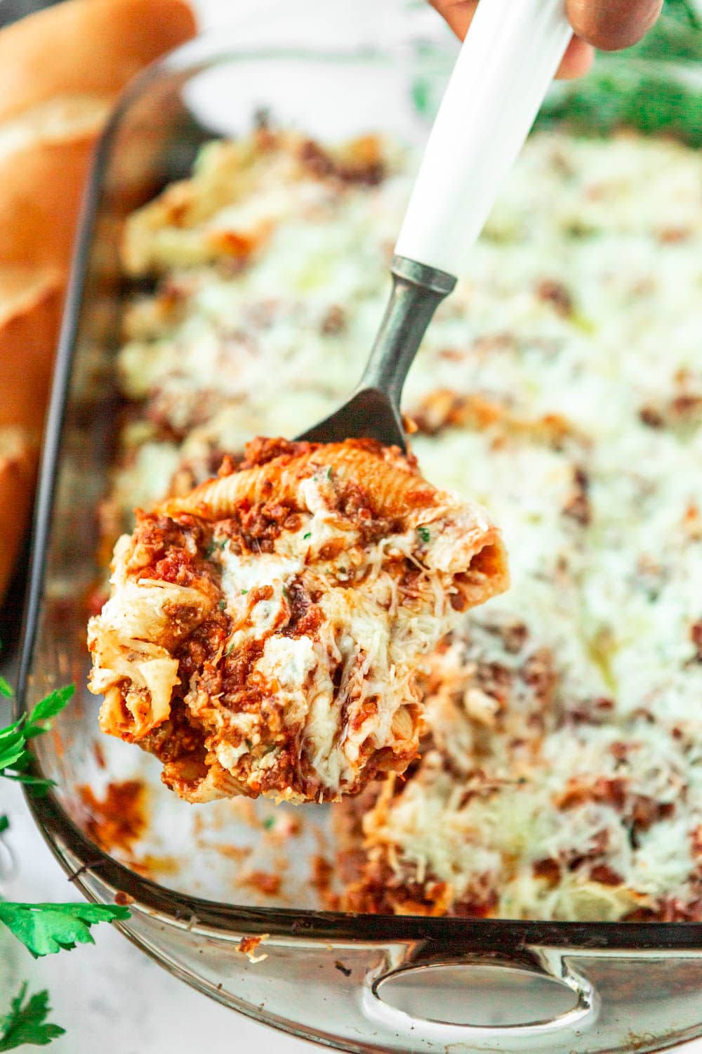 stuffed pasta shells in a 9x13 baking dish with a spoon lifting 3 stuffed shells out of the baking dish. 
