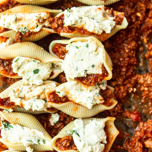 twelve shells filled with ricotta cheese on top of meat sauce