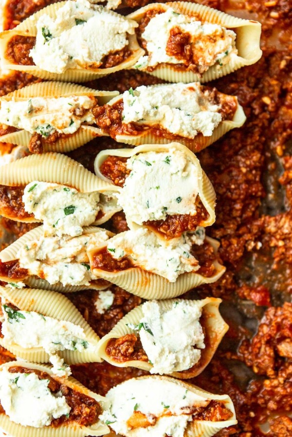 twelve shells filled with ricotta cheese on top of meat sauce
