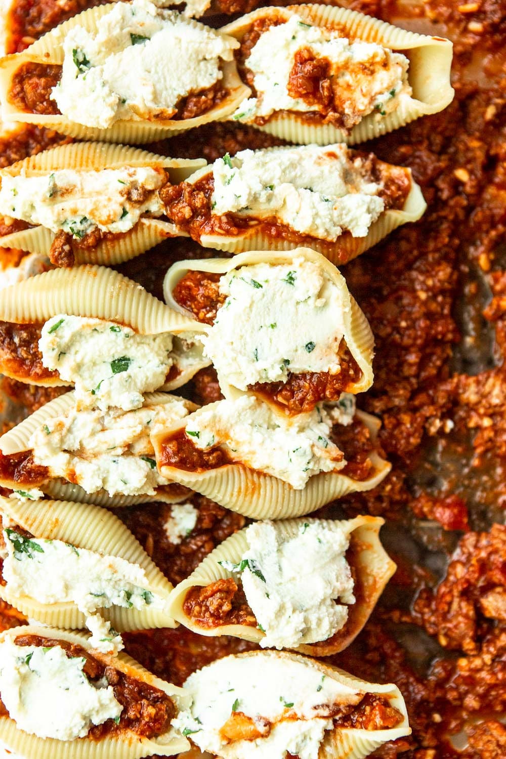 twelve shells filled with ricotta cheese on top of meat sauce 