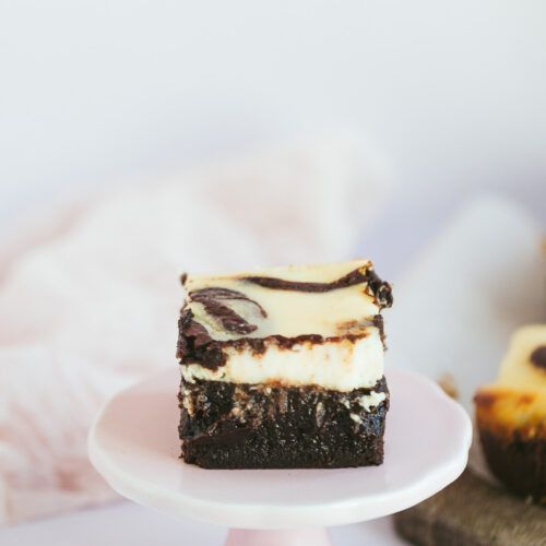 a squared cheesecake brownie slice on a pink cake stand