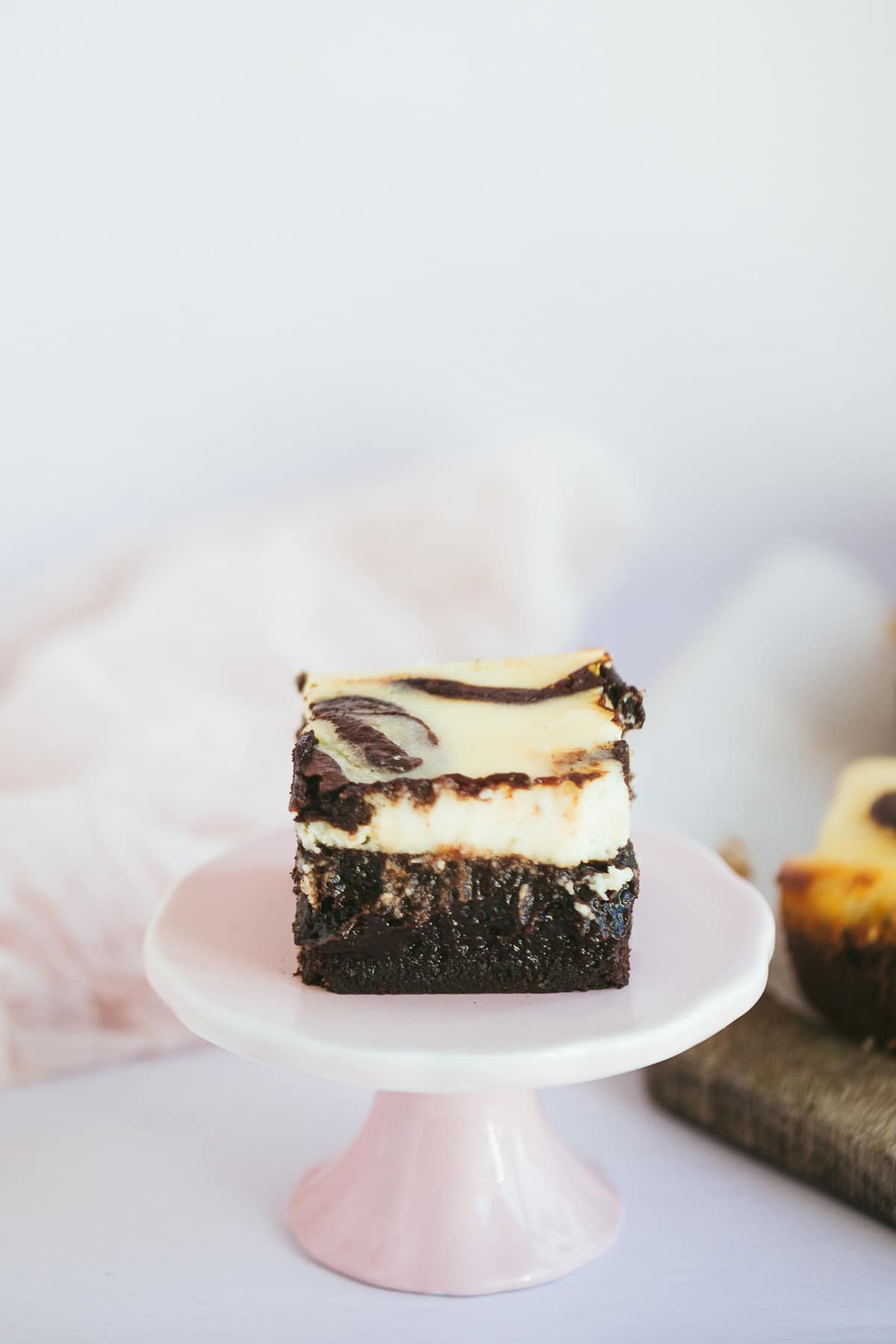 a squared cheesecake brownie slice on a pink cake stand