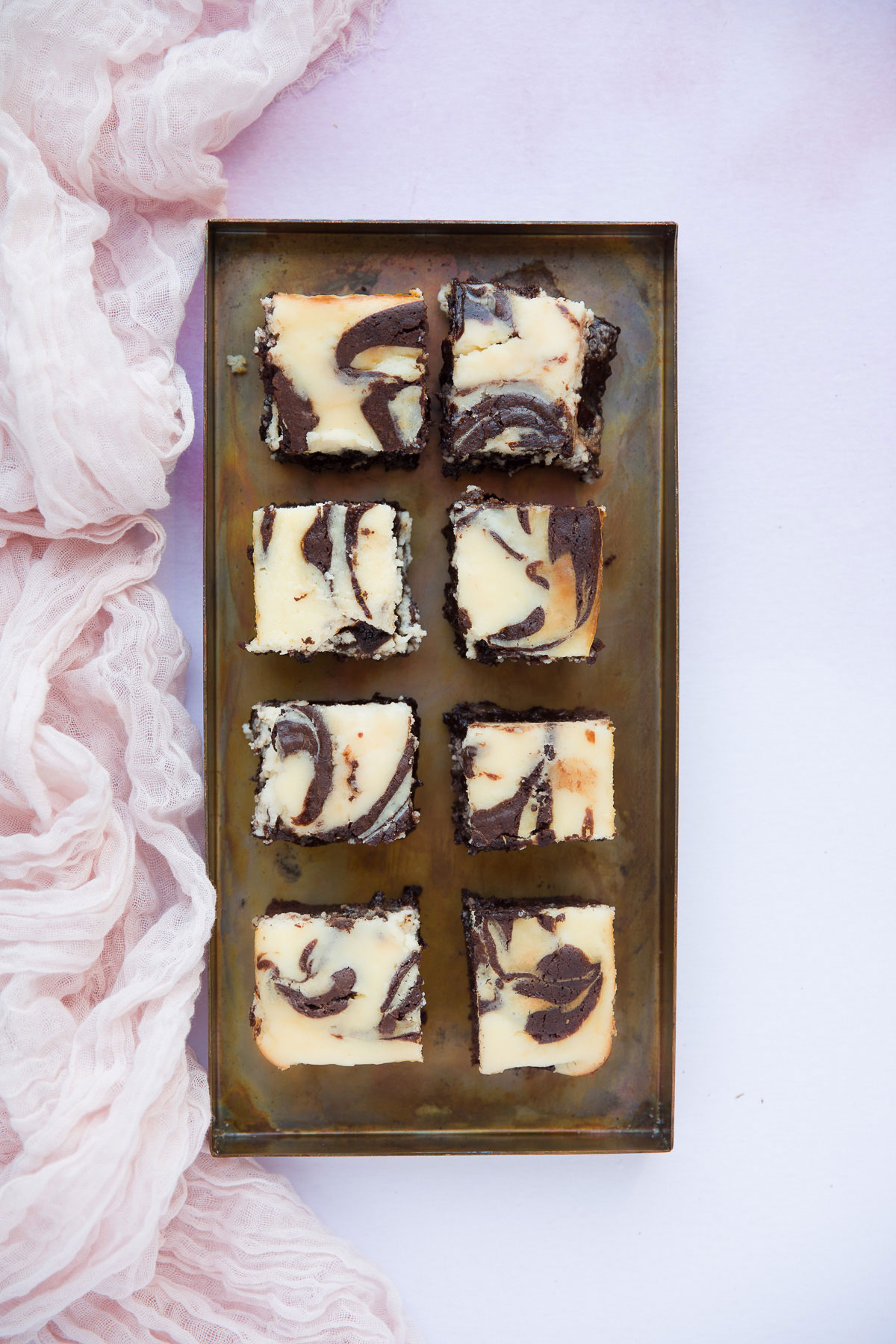 eight brownies on a serving dish with a pink towel on the side. 