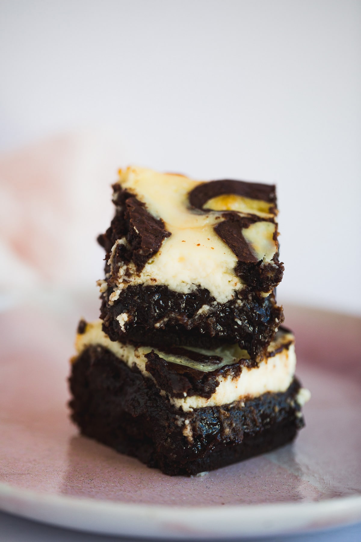 two cheesecake brownies stacked on top of a pink plate. 