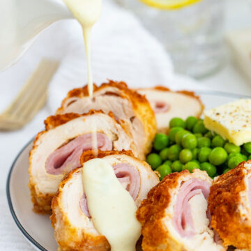 chicken cordon bleu on a plate with sauce on top and green peas on the side.