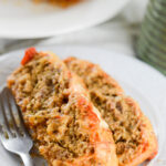 two slices of meatloaf parmesan on a white plate with a fork on the side.