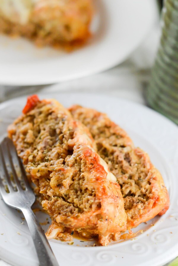two slices of meatloaf parmesan on a white plate with a fork on the side.