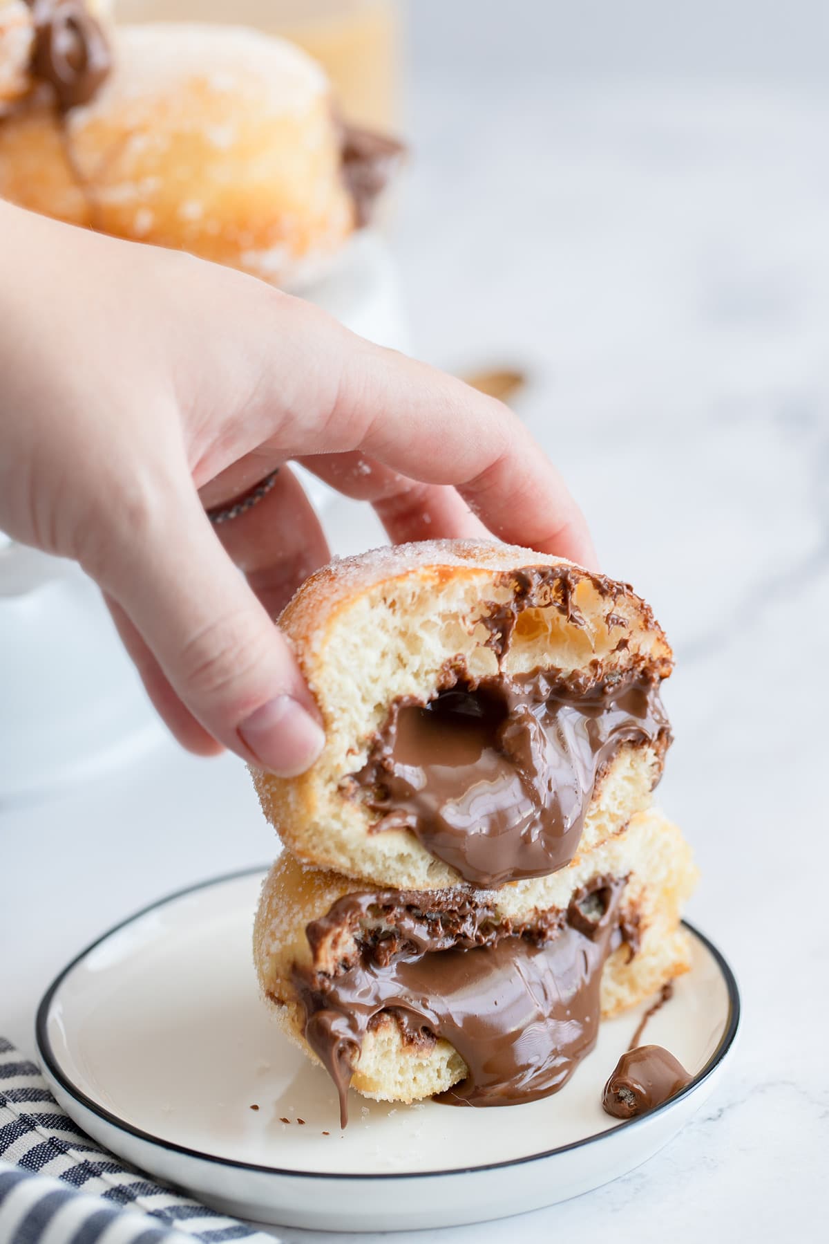 two nutella doughnuts on a small plate with nutella coming out of the donuts and a hand holding the donuts.