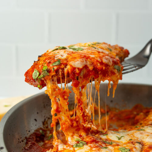 a spatula lifting chicken parmesan from the skillet.