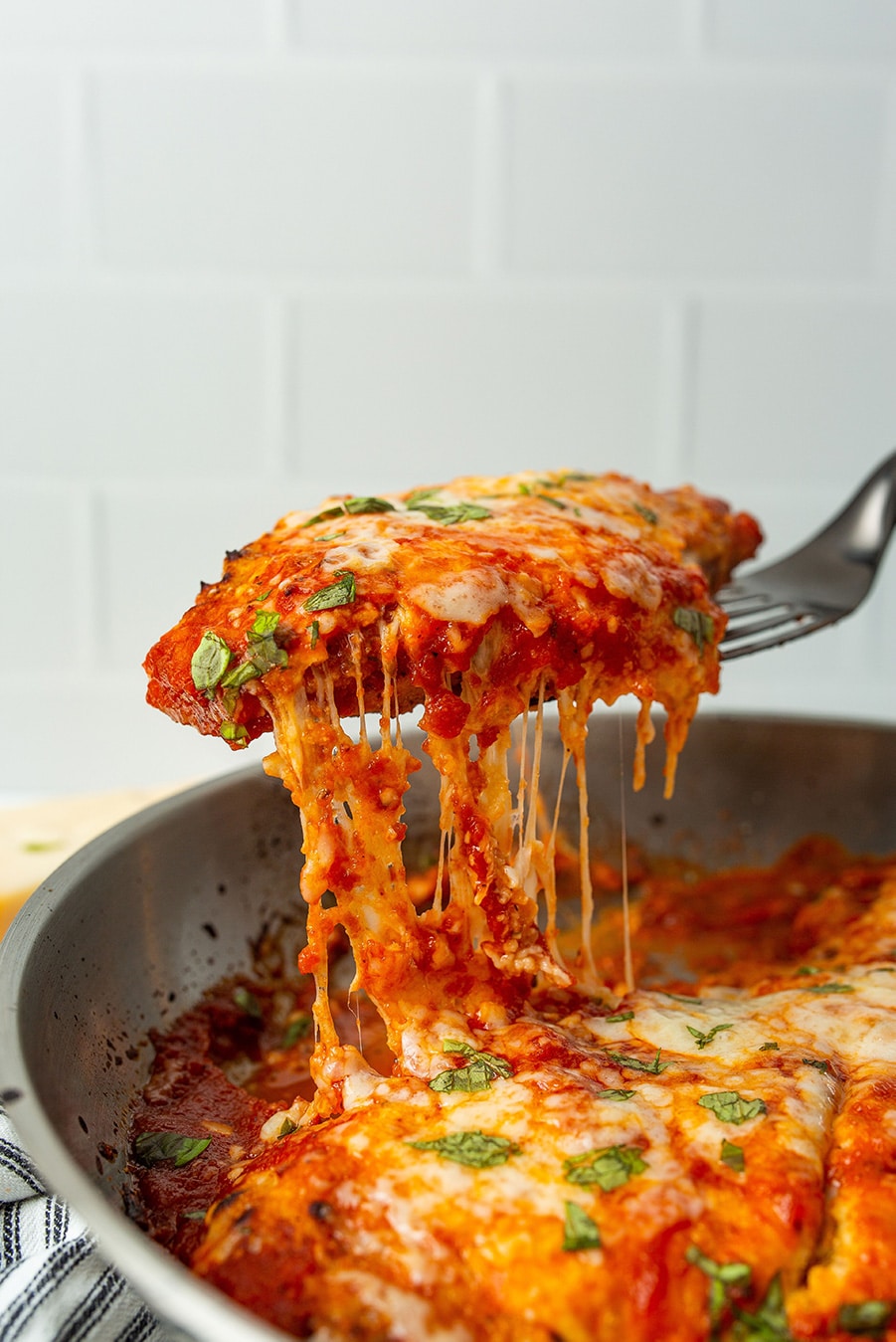 a spatula lifting chicken parmesan from the skillet. 