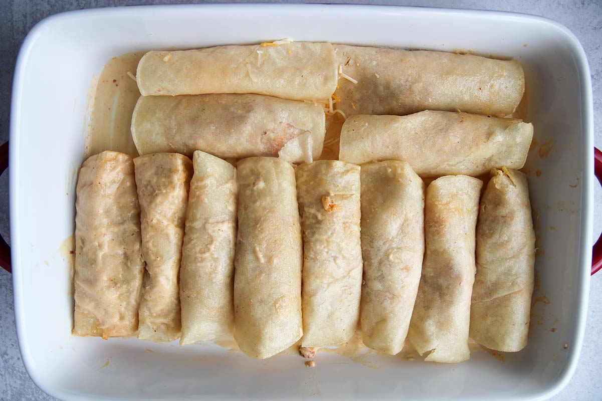 twelve rolled corn tortillas in a white casserole dish.