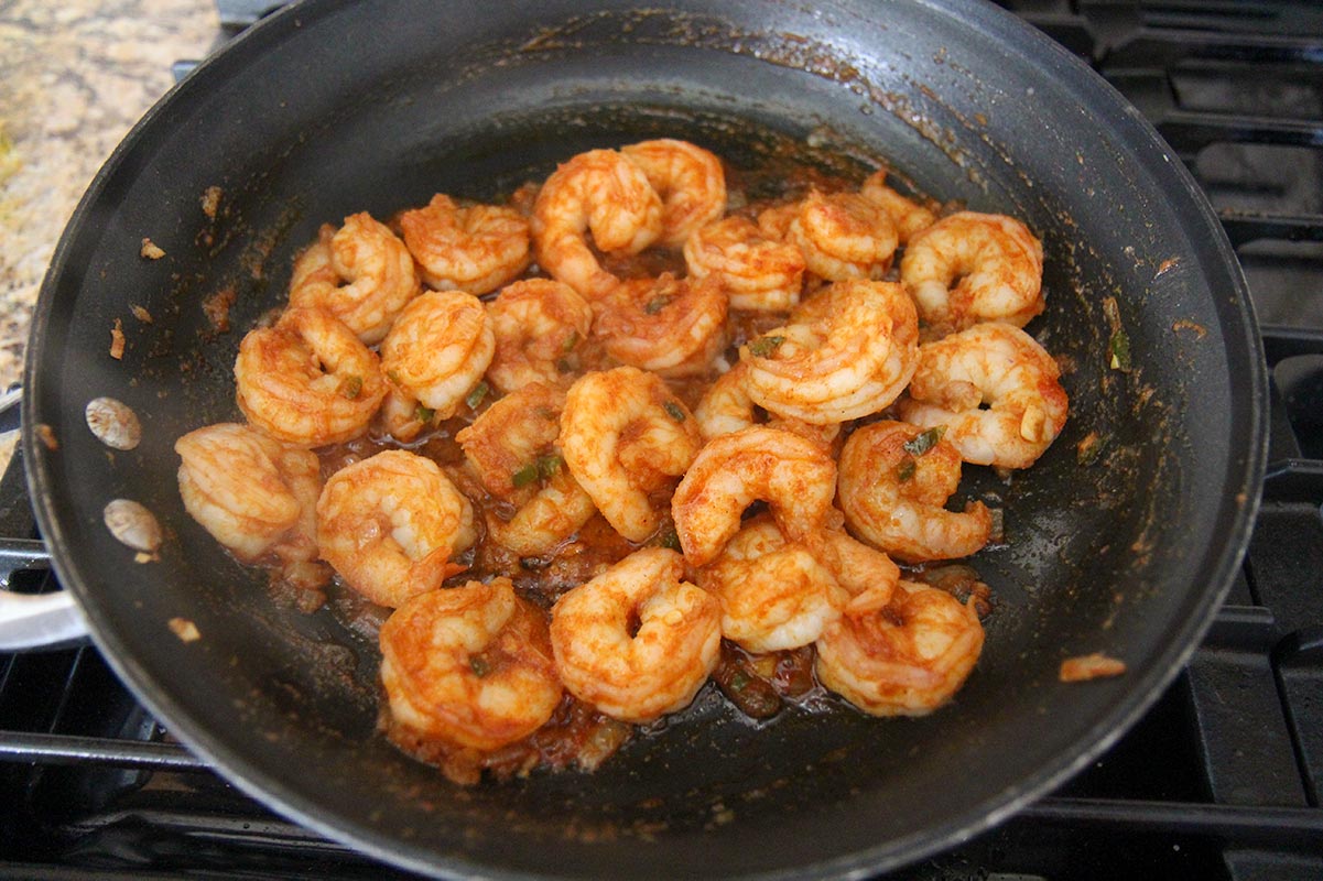 shrimp cooking in a black skillet on a stove top. 