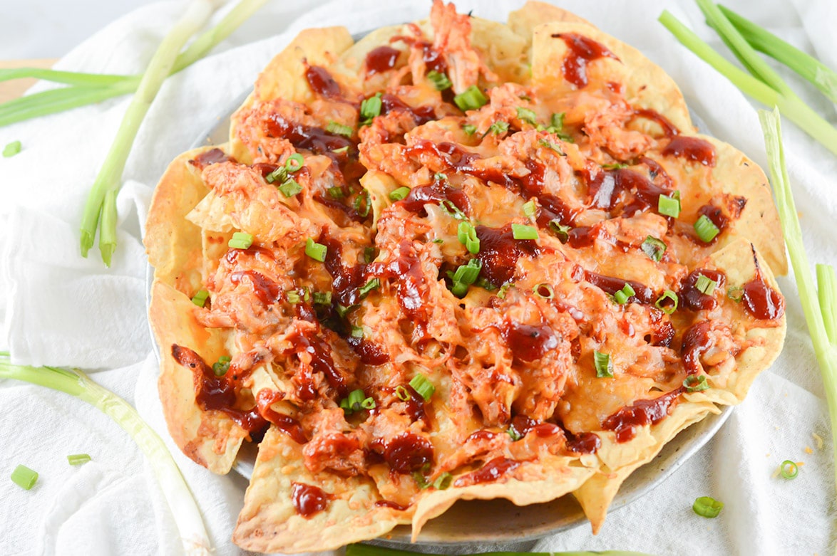 a large platter with barbecue chicken nachos and scallions on the side 