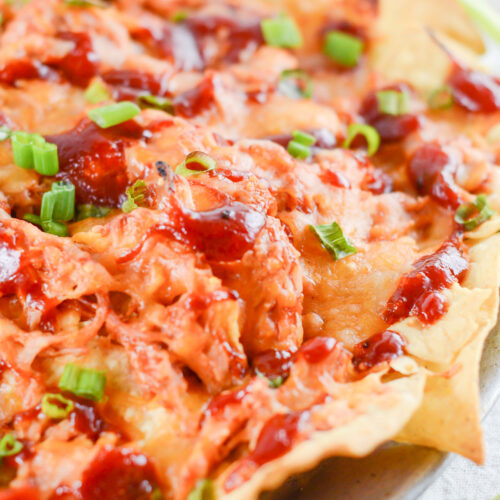 nachos with pulled chicken, bbq sauce, cheese, and scallions on a plate.