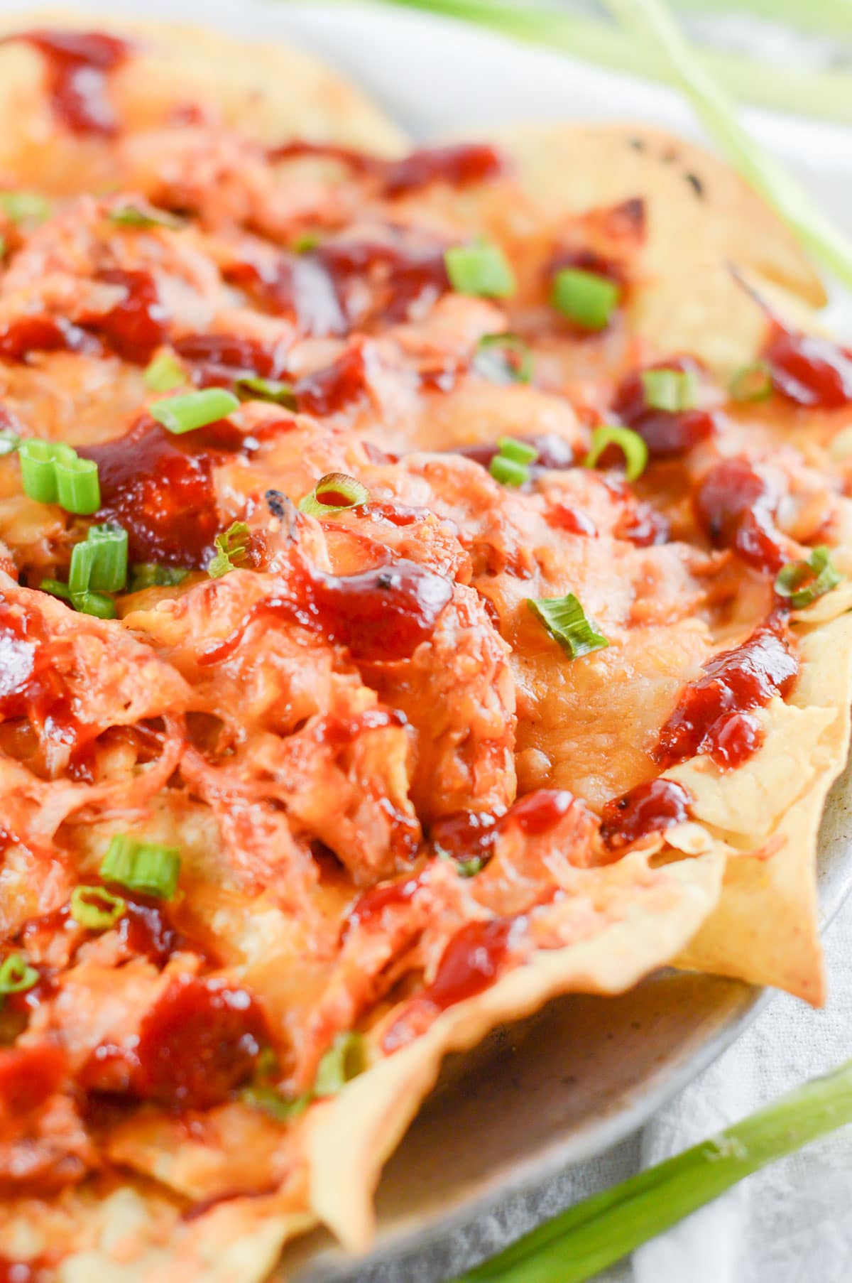 nachos with pulled chicken, bbq sauce, cheese, and scallions on a plate.