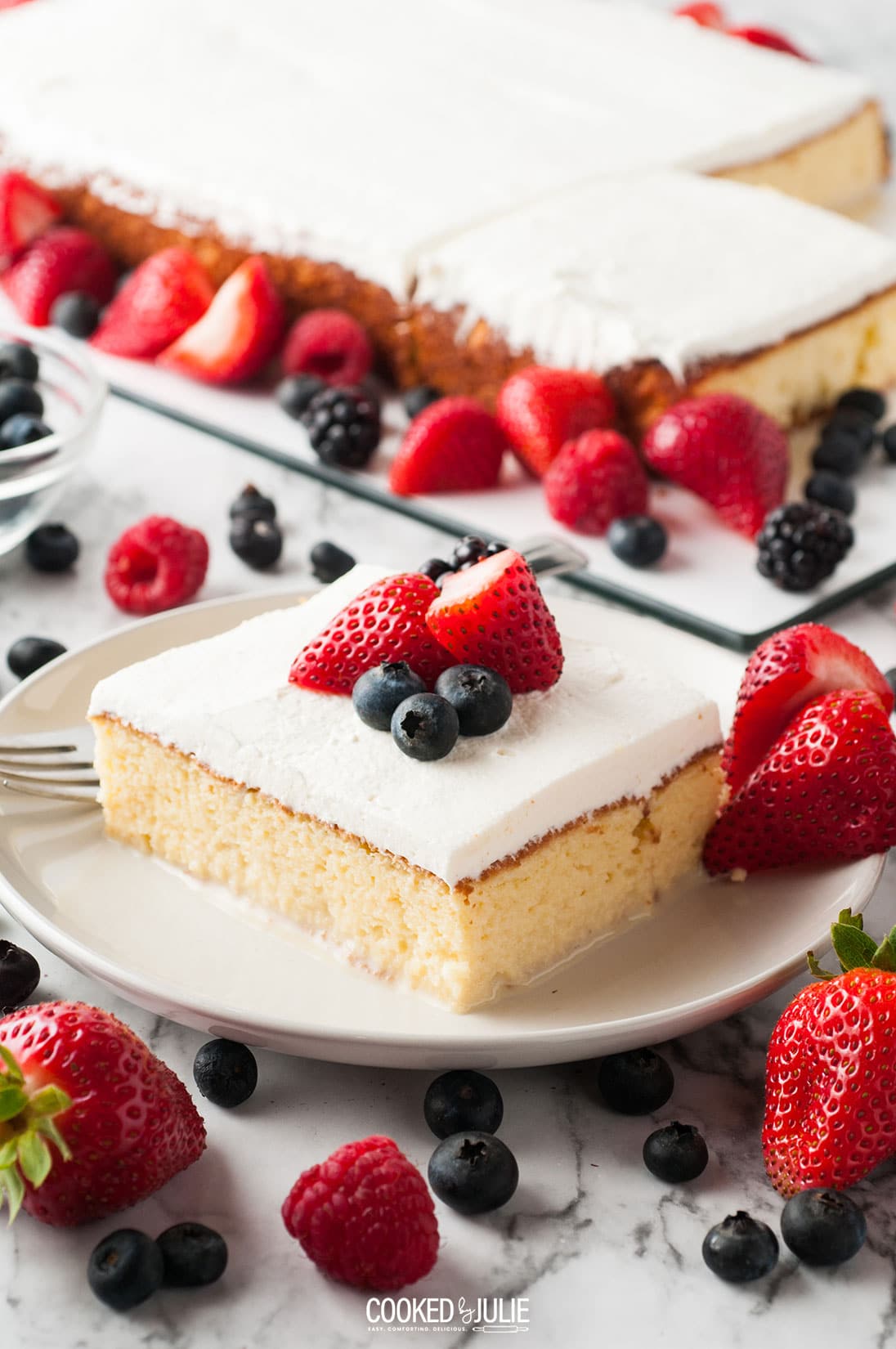 a slice of tres leches cake on a white plate with berries 