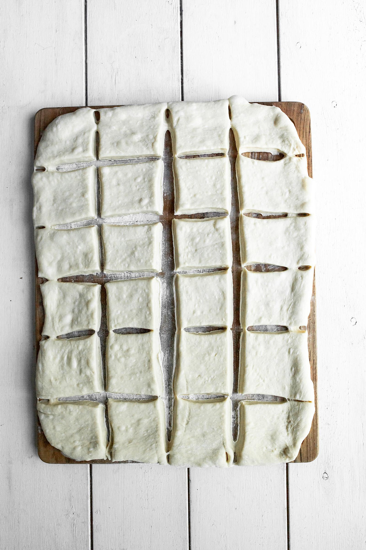 twenty four squares of raw dough on a wooden board.