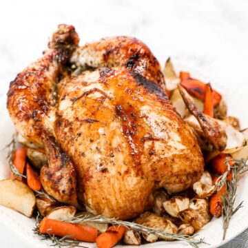 a whole honey roasted chicken on a platter with herbs and carrots