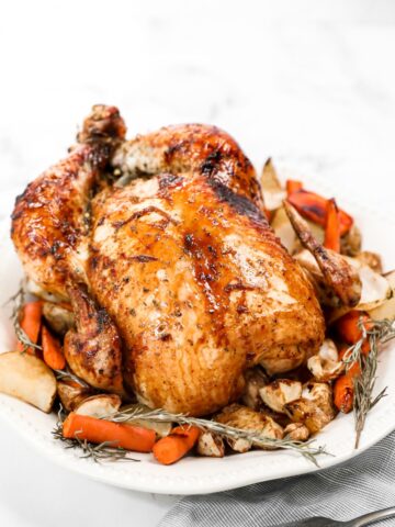 a whole honey roasted chicken on a platter with herbs and carrots