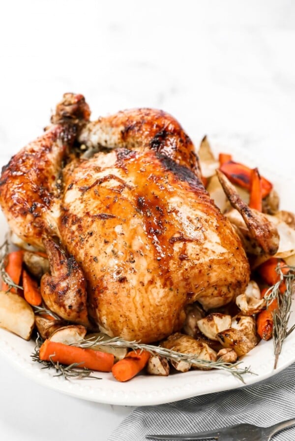 a whole honey roasted chicken on a platter with herbs and carrots