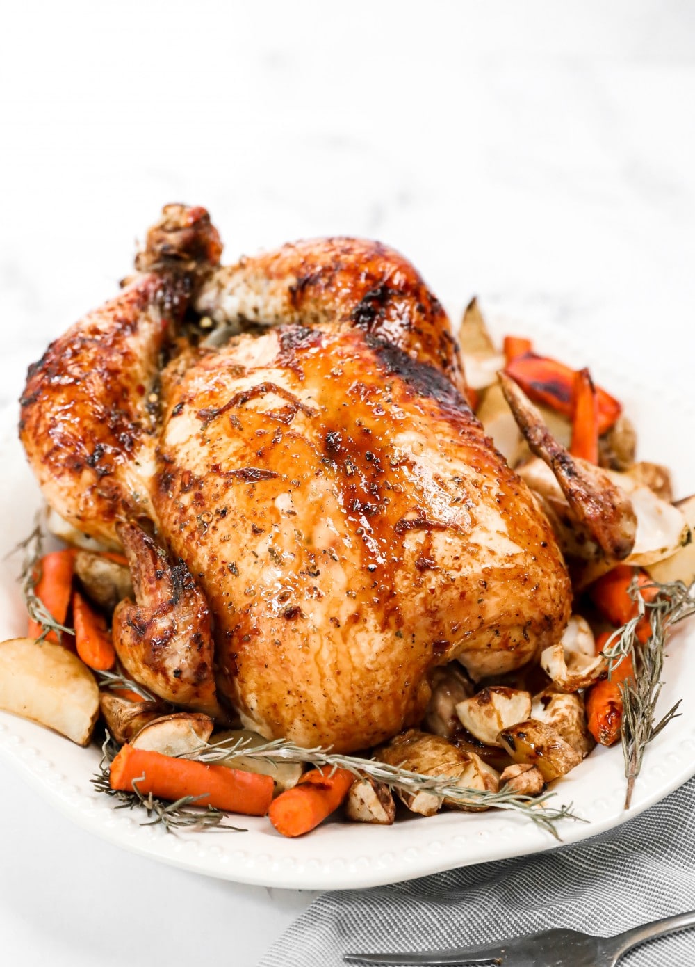 a whole honey roasted chicken on a platter with herbs and carrots