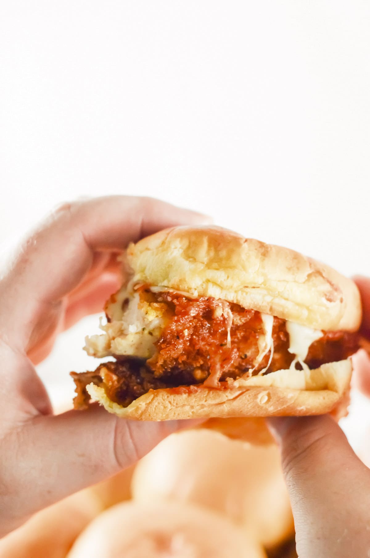 two hands holding up a chicken parm slider. 