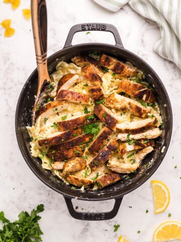 Cajun chicken, farfalle pasta, parsley, and a wooden spoon in a black skillet.