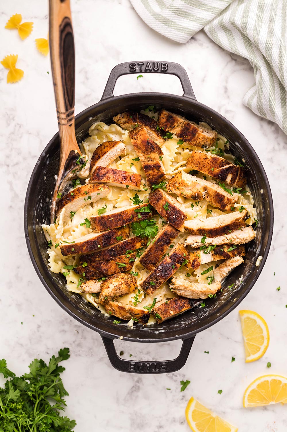 Cajun chicken, farfalle pasta, parsley, and a wooden spoon in a black skillet.