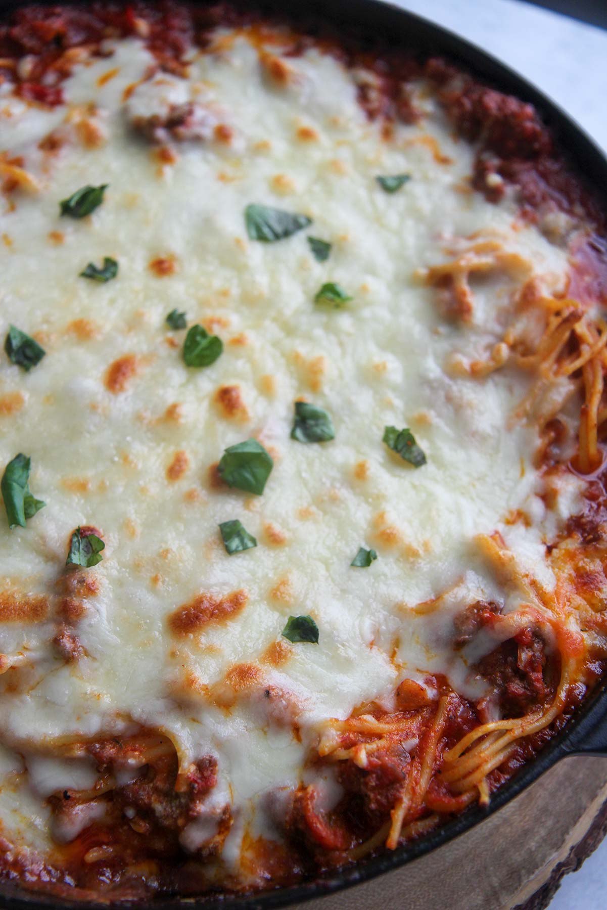 baked spaghetti with melted cheese and fresh basil up close. 