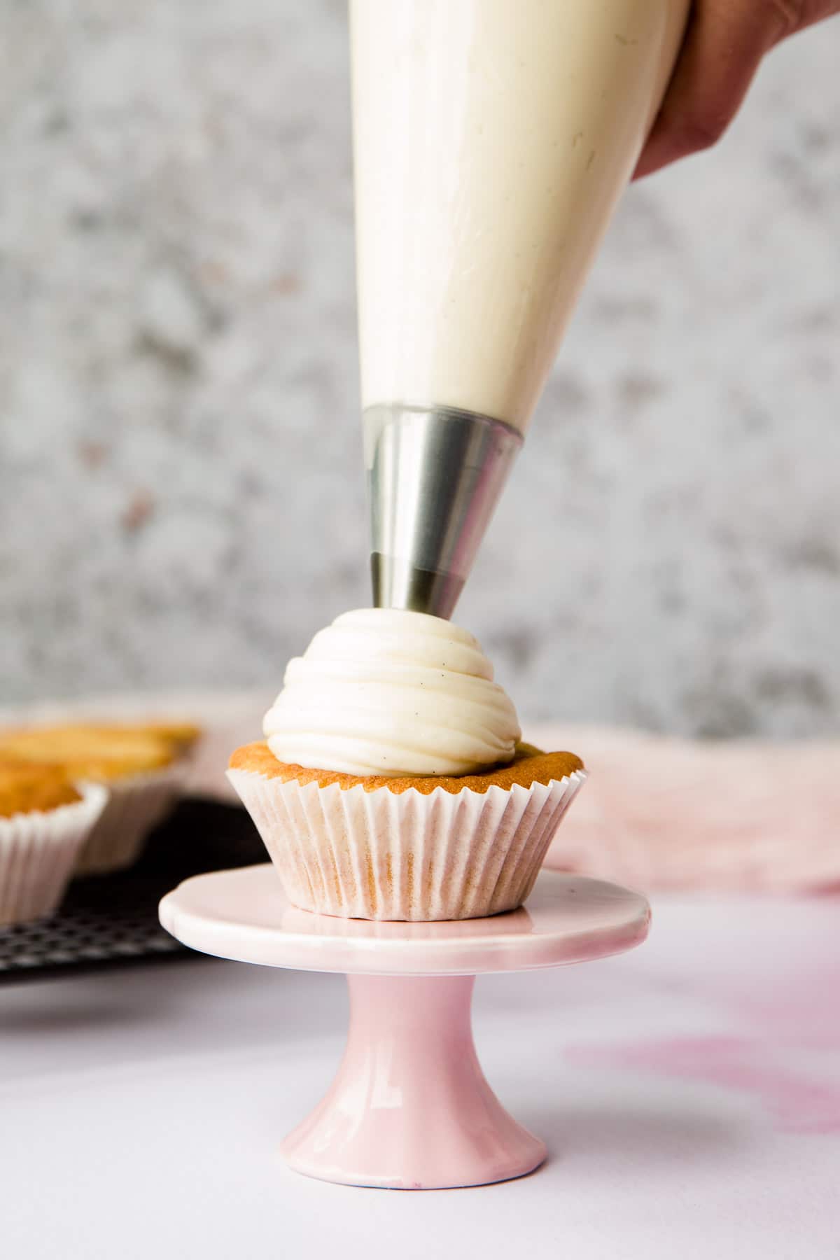 a cupcake being frosted with a piping bag and star tip. 