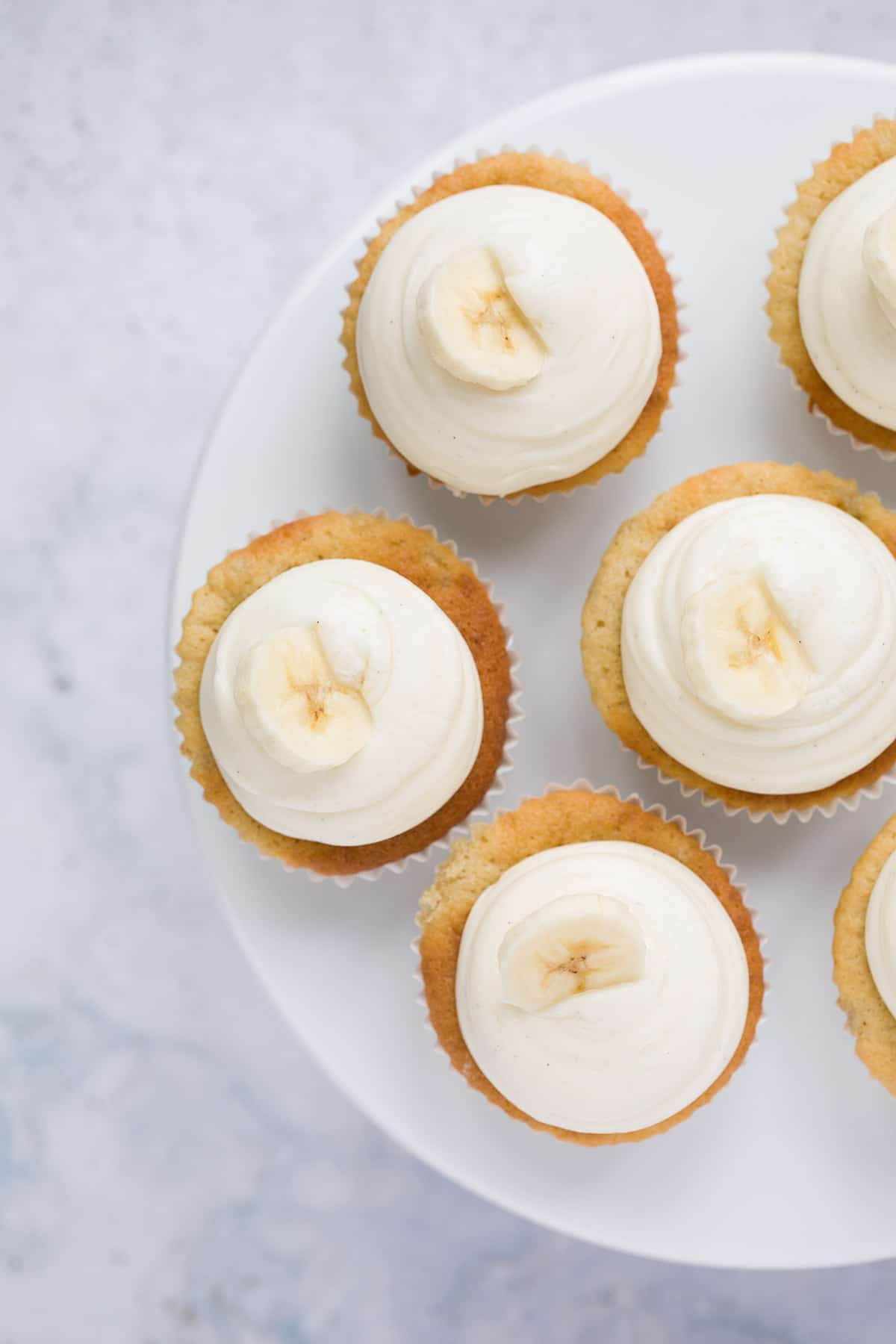 six banana cupcakes with cream cheese frosting on a cake stand 