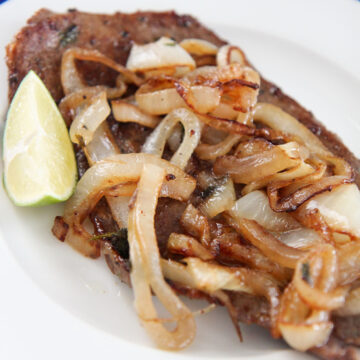 Cuban style steak and onions on a white plate with a lime wedge on the side.