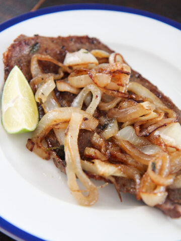 Cuban style steak and onions on a white plate with a lime wedge on the side.