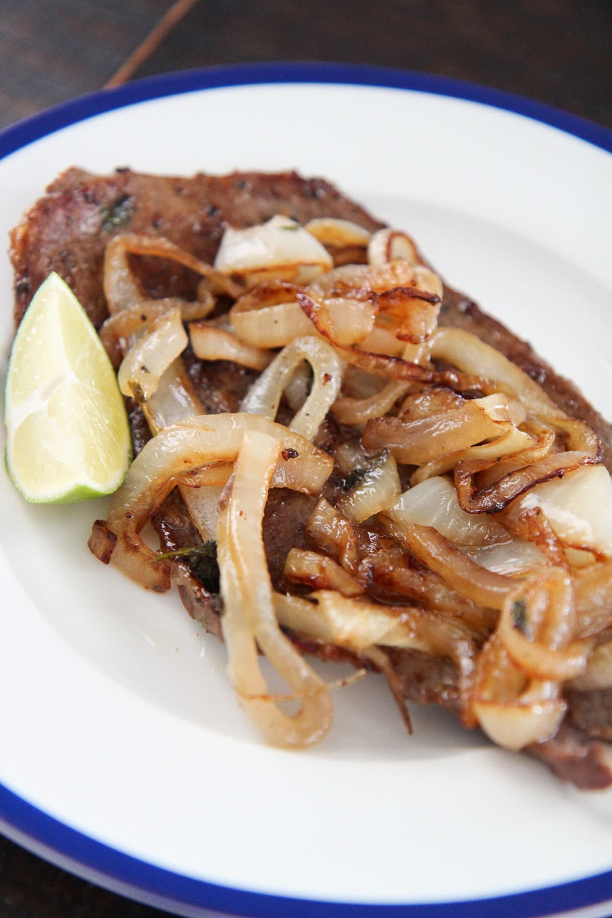 Cuban style steak and onions on a white plate with a lime wedge on the side. 