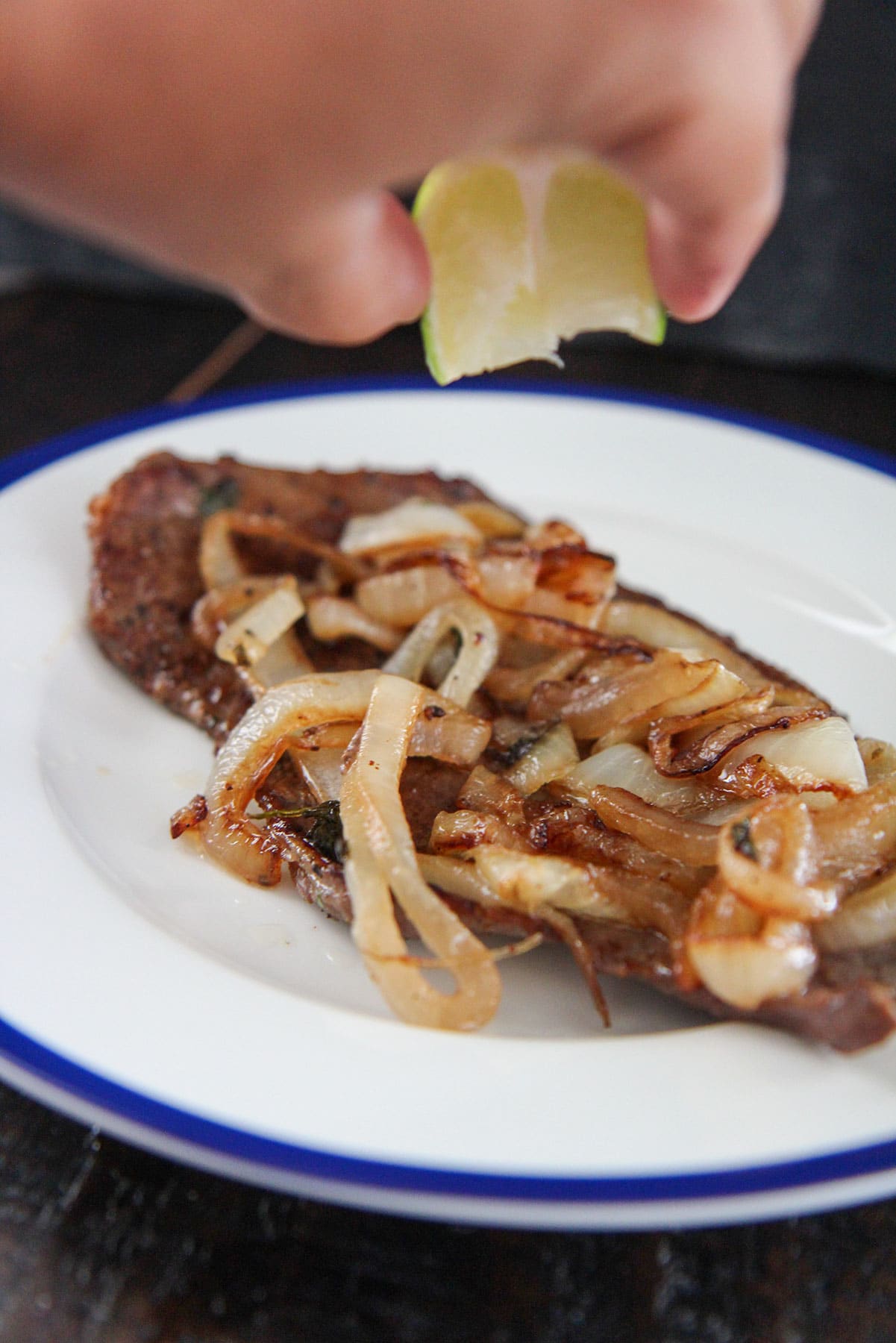 bistec encebollado with a hand squeezing lime juice over it. 
