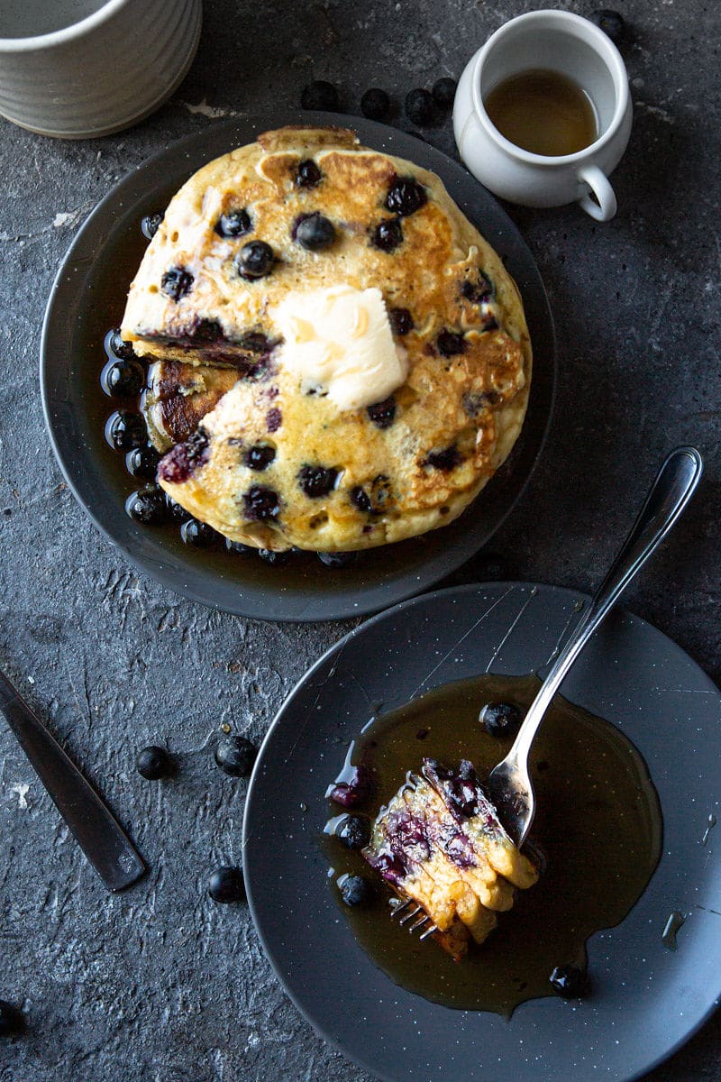 a short stack of blueberry pancakes and a small plate with a fork and four pancake slices. 