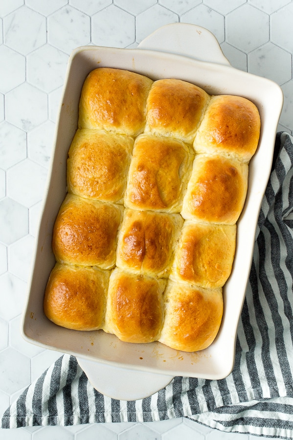 a dozen baked dinner rolls in a white baking dish on top of a white and blue kitchen towel.
