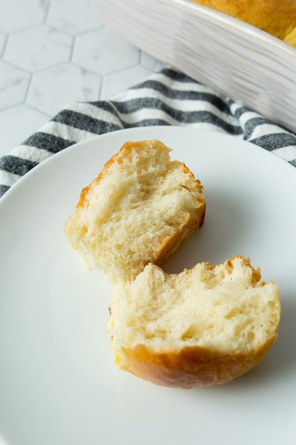 one bread roll split in half on a small white plate with a blue and towel on the side. 