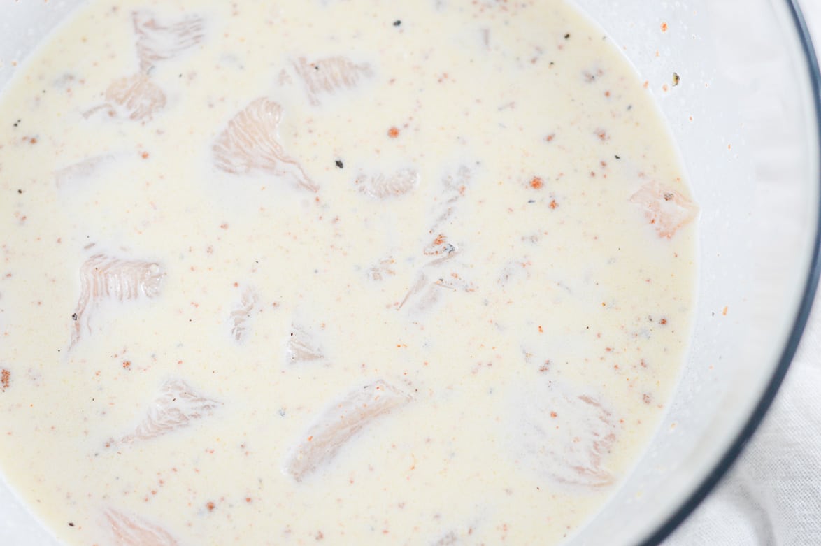 chicken coated in buttermilk in a large glass bowl 