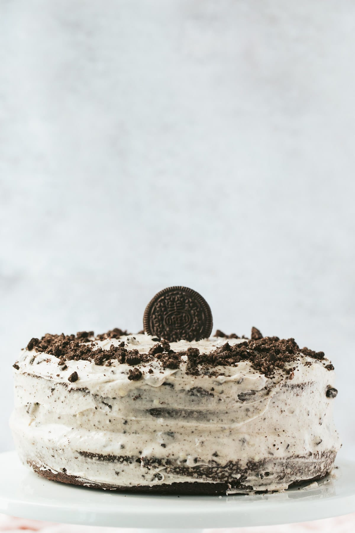 a two layer oreo cake with one oreo cookie on top and crumbs around the sides. A light background. 