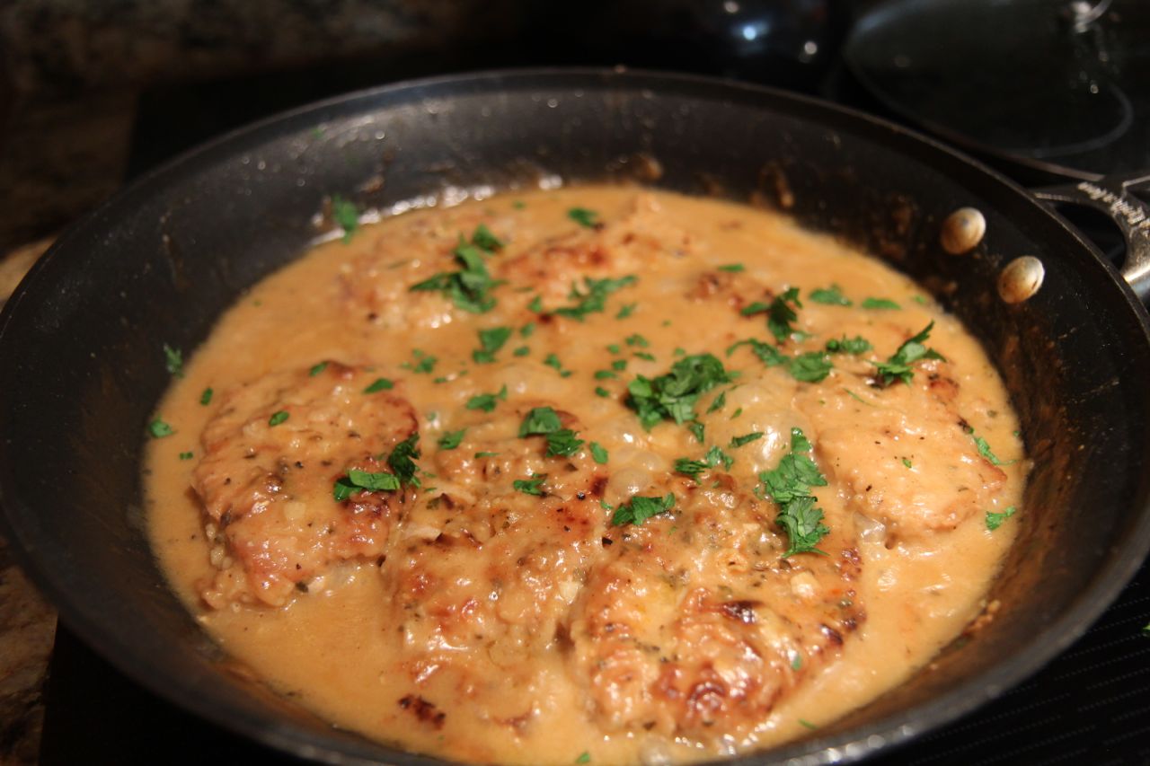 smothered pork chops, parsley, in a black skillet. 