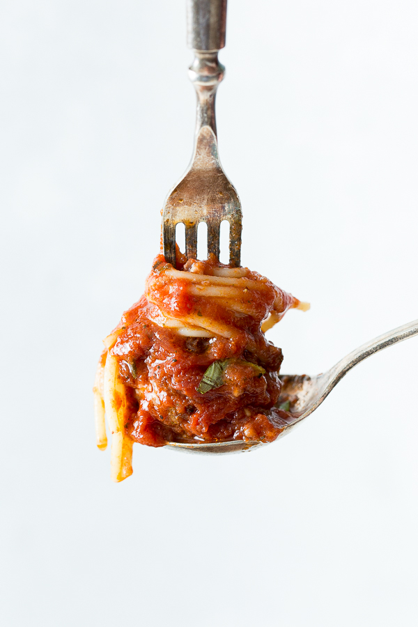 a spoon holding a small portion of spaghetti and a meatball with a fork on top. 