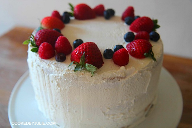 Triple layer triple berry cake with light vanilla frosting topped with fresh summer berries