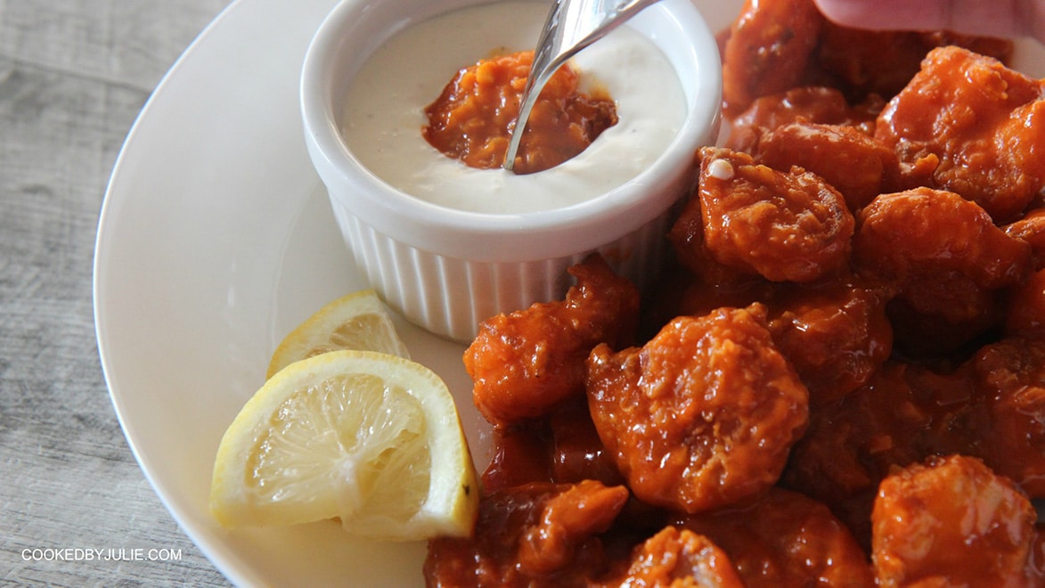 buffalo shrimp in a white bowl and one shrimp dipped in blue cheese dip with a fork. 