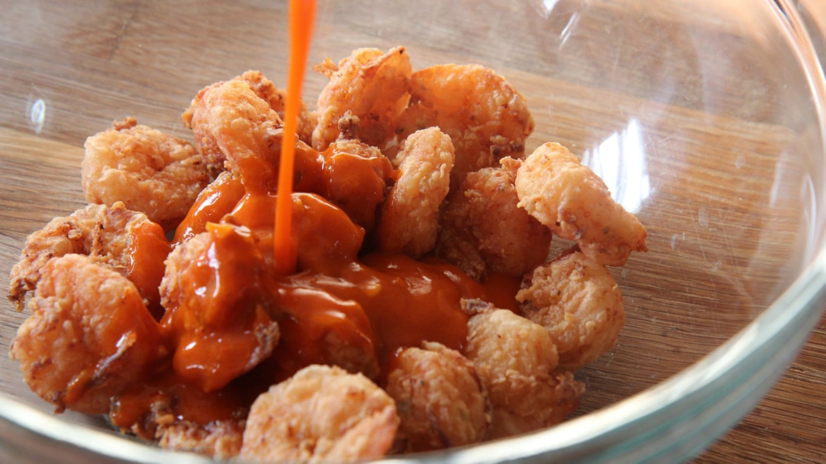 fried shrimp in a bowl with buffalo sauce poured on top