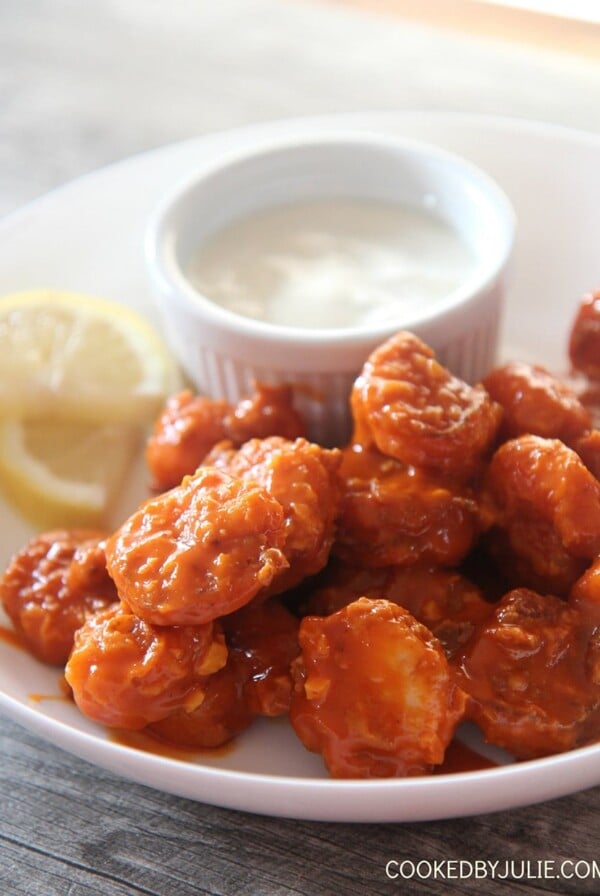 crispy buffalo shrimp with lemon slices and a side of bleu cheese dip in a white bowl.