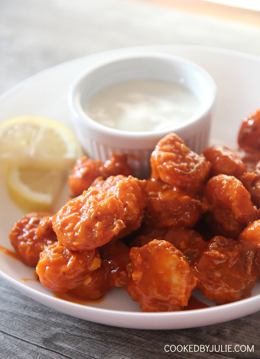 crispy buffalo shrimp with lemon slices and a side of bleu cheese dip in a white bowl.